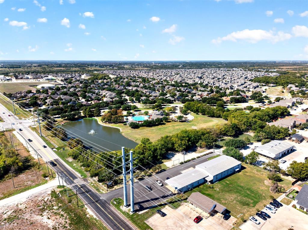 Aerial perspective of property featuring a pond with water feature, paved parking area, and multi-bay structure with metal roofing