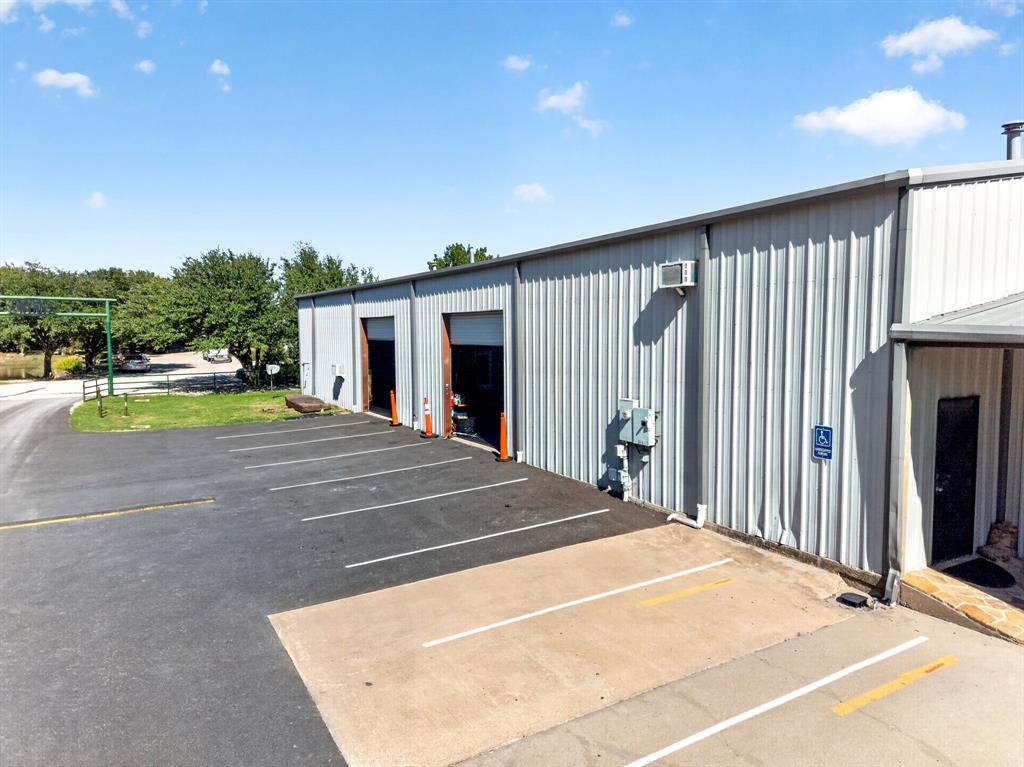 Metal-paneled exterior building featuring two wide bay entrances, paved parking area with designated spaces, and established exterior lighting