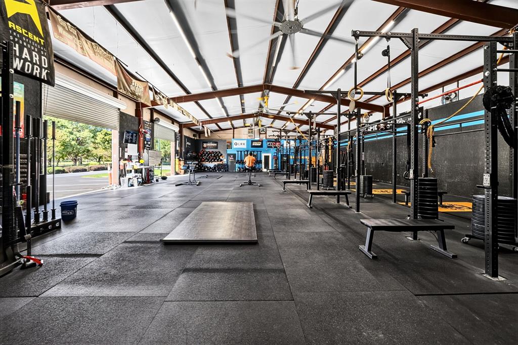 Open-concept industrial space featuring a vaulted ceiling with exposed steel beams, high-capacity ceiling fans, recessed lighting, and durable rubberized flooring