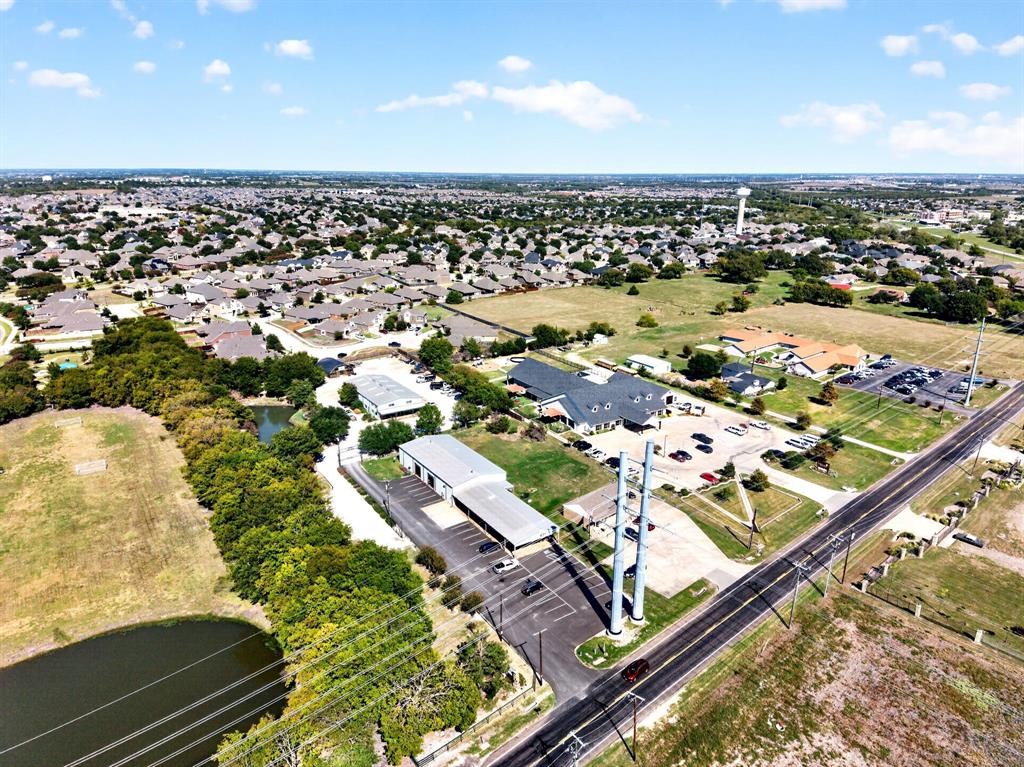 Aerial perspective featuring multiple industrial-style metal structures, paved parking areas, covered canopy parking, and a natural pond situated on a large lot