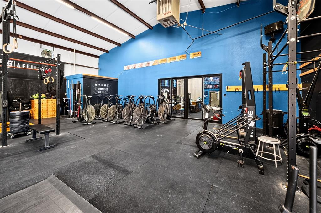 Open-concept interior space featuring high vaulted ceilings, durable rubberized flooring, mounted industrial-style climate control unit, and extensive glass door entry