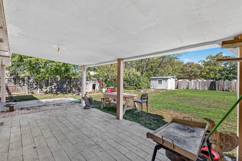 Covered patio featuring wood-finish tile flooring and support columns, expansive backyard, and perimeter wood fencing