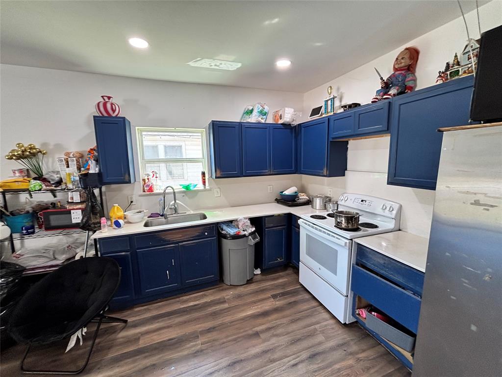 Kitchen featuring navy cabinetry, solid-surface countertops, wood-finish flooring, recessed lighting, and a stainless steel sink with a high-arch faucet