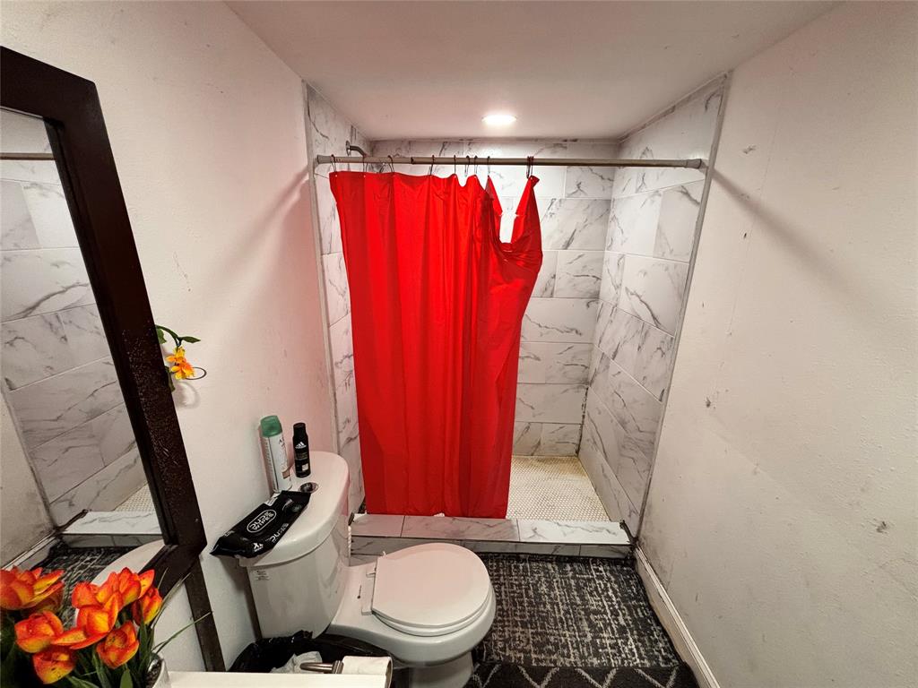 Bathroom featuring a walk-in shower with large-format, light-toned stone-patterned wall tile and a built-in shower curb