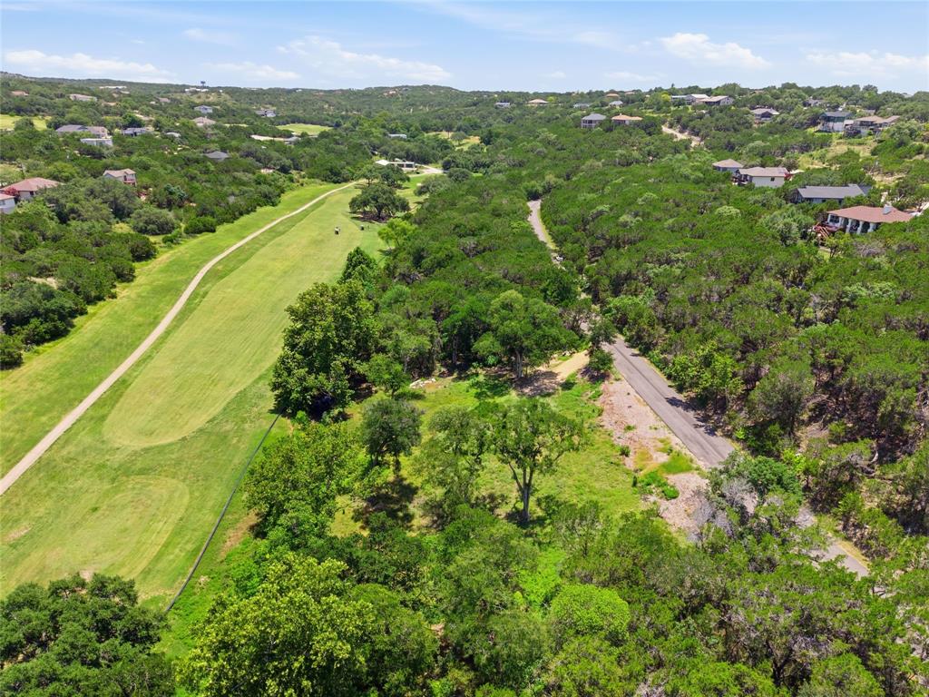 Aerial perspective of a sloping lot featuring mature trees, native brush, paved road access, and proximity to maintained green space
