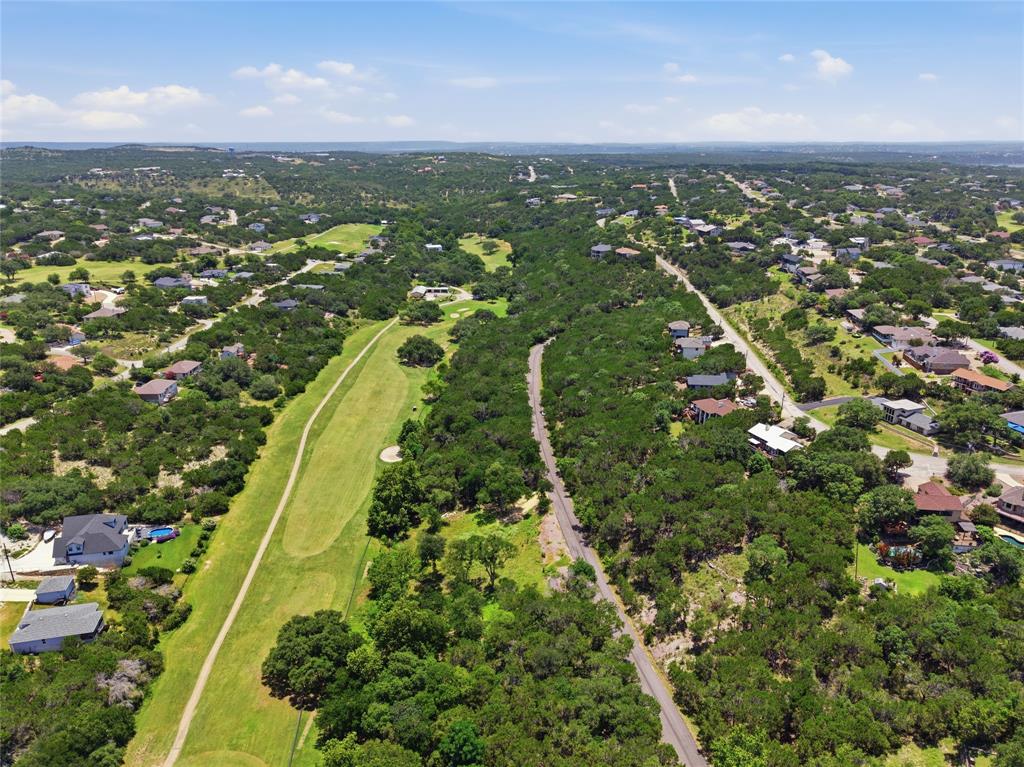 Aerial perspective showcasing a sprawling landscape with extensive native tree coverage, manicured grass fairways, and paved thoroughfares