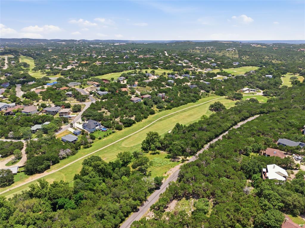 Aerial perspective of a sprawling landscape featuring expansive green terrain, dense clusters of mature trees, winding paved roads, and residential properties