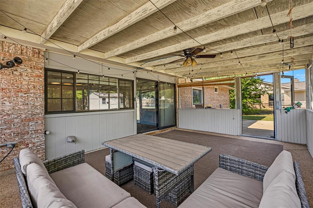 Covered patio featuring an exposed-beam ceiling, brick siding, concrete flooring, and a ceiling fan