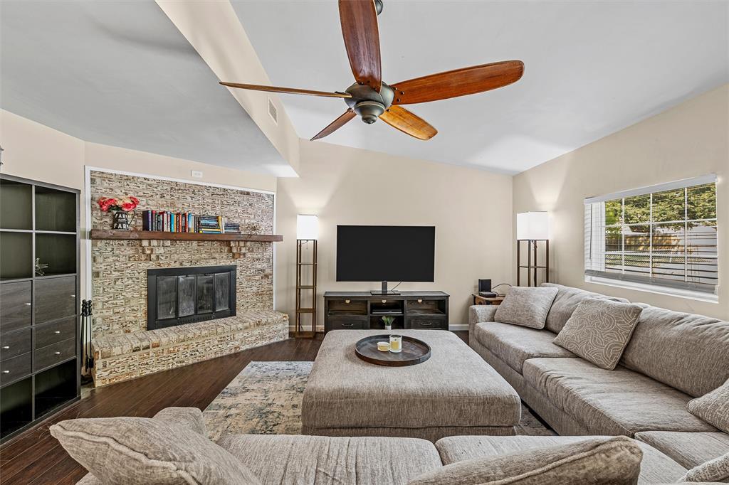 Living area featuring vaulted ceilings, wood-finish flooring, a stacked-stone fireplace with a timber mantel, and a five-blade ceiling fan