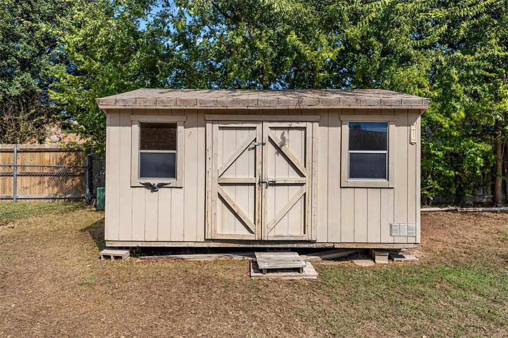 Outdoor storage structure featuring tan composite siding, two single-pane windows, double-door entry, and a pitched roof