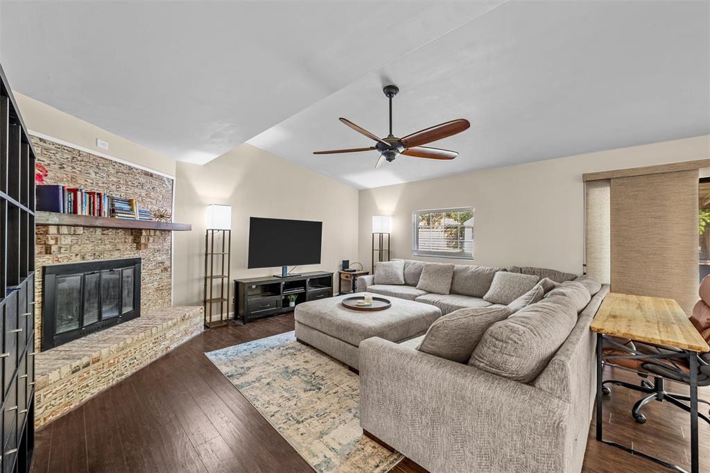 Living area featuring a floor-to-ceiling stone-faced fireplace with a natural wood mantel, wood-finish flooring, vaulted ceilings, and a multi-blade ceiling fan