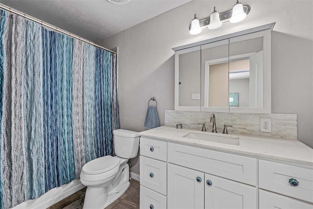 White vanity with rectangular sink, stone-finish countertop, three-paneled medicine cabinet, horizontal tile backsplash, and three-light fixture