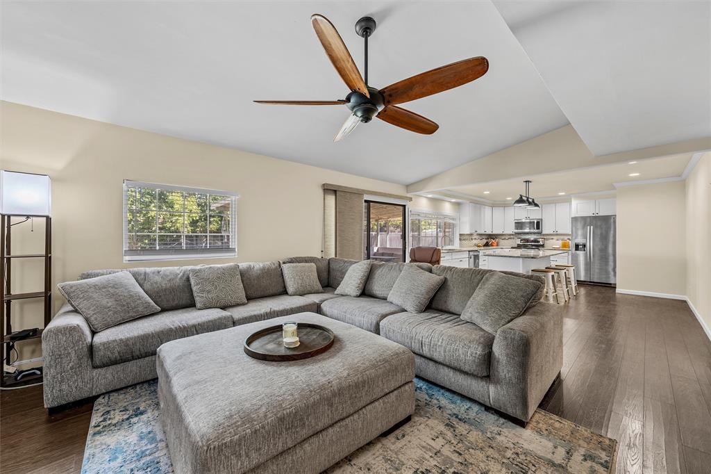 Vaulted ceiling with a wood-blade ceiling fan, dark wood-finish flooring, and open-concept kitchen featuring white cabinetry and recessed lighting
