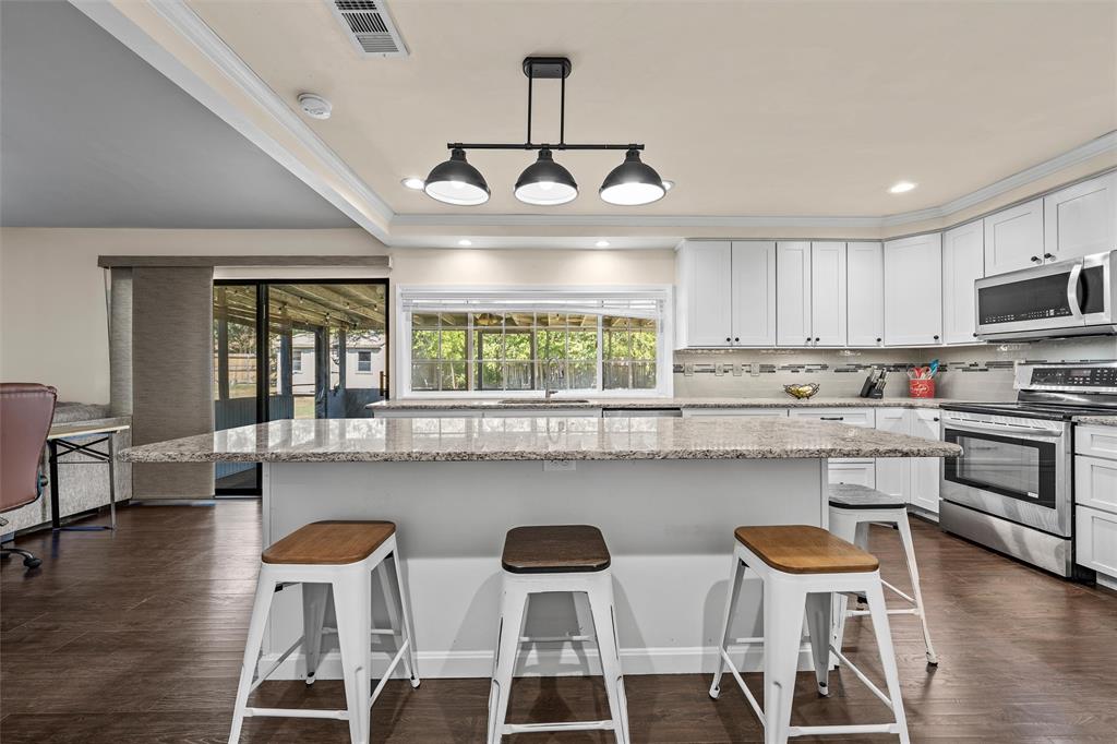 Kitchen featuring a stone-topped island with seating, white cabinetry, stainless steel appliances, and a three-light pendant fixture over wood-finish flooring