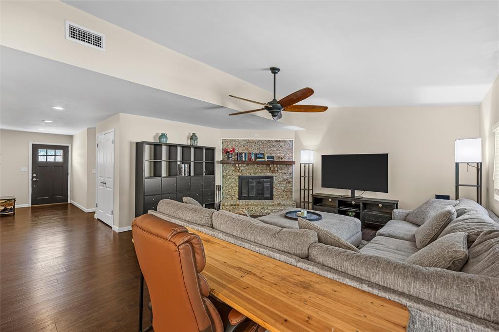Living area featuring wood-finish flooring, a corner brick fireplace with a wood mantel, and a ceiling fan