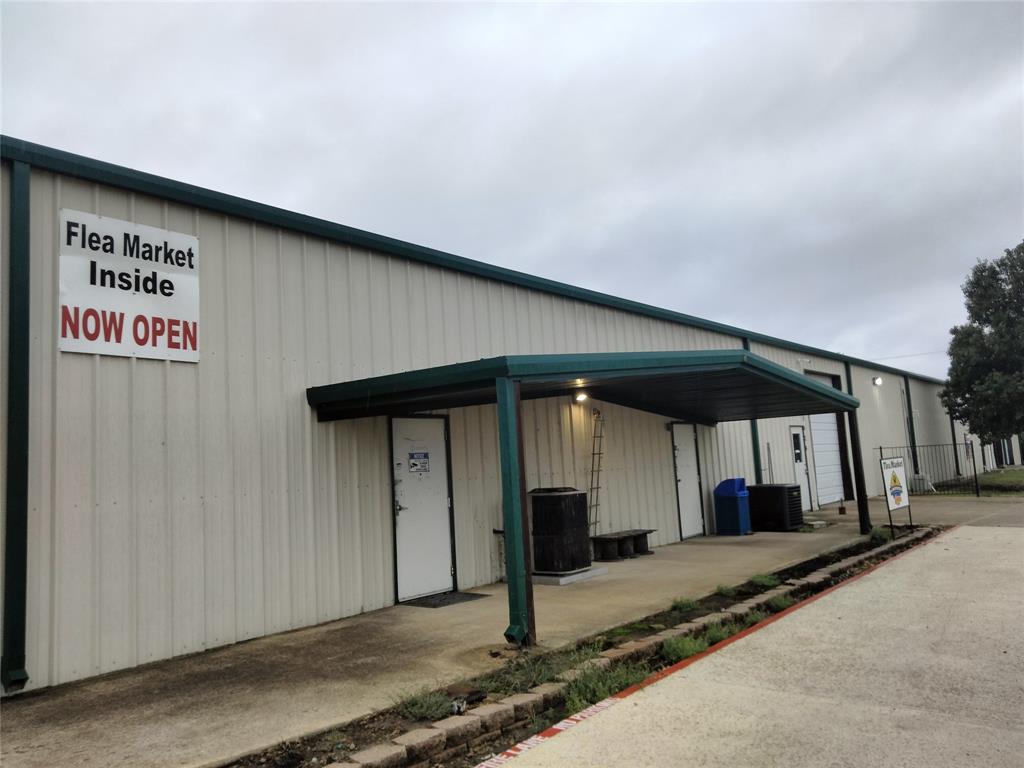 Industrial-style exterior featuring corrugated metal siding, an expansive paved concrete apron, and a covered entryway with a metal overhang