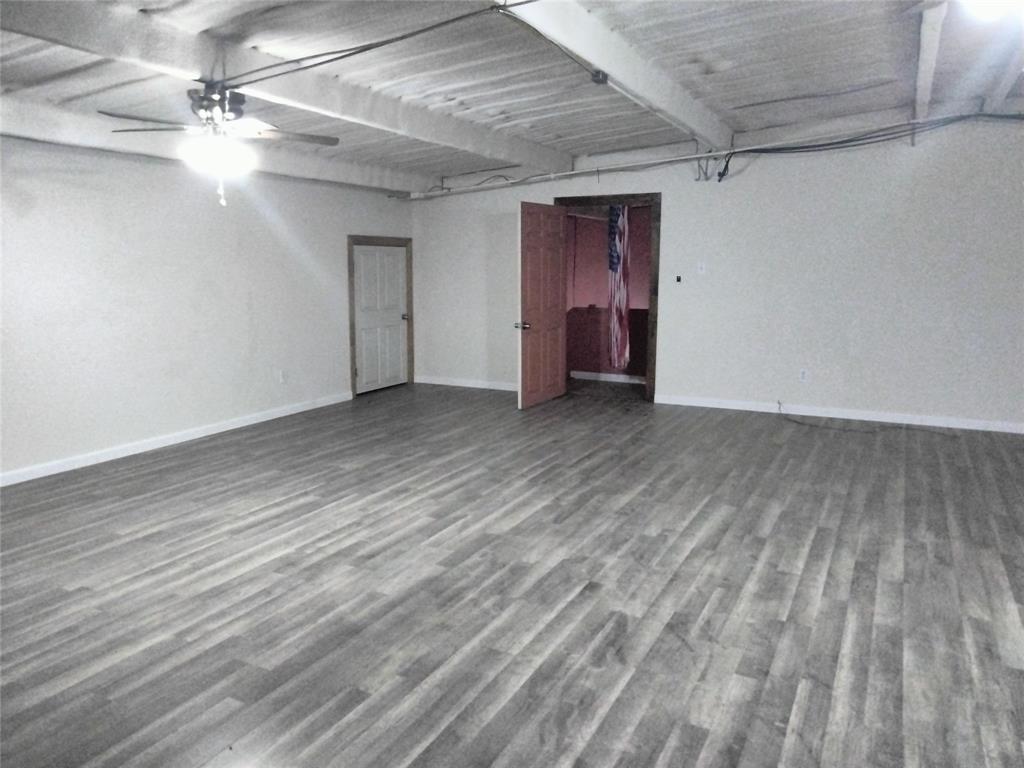 Open-concept interior featuring wood-finish flooring, white exposed joist ceilings, and a ceiling fan with integrated lighting