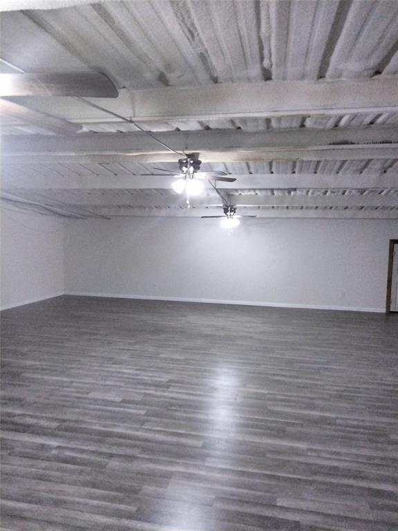 Expansive interior space featuring wood-finish flooring, exposed structural ceiling beams, and dual ceiling fans with integrated lighting