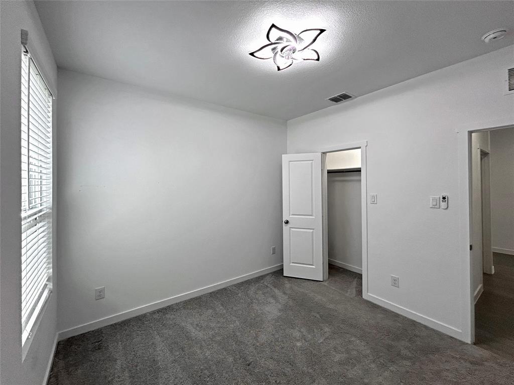 Interior space featuring neutral-toned carpeting, a floral-inspired flush-mount ceiling light fixture, horizontal window blinds, and a built-in closet