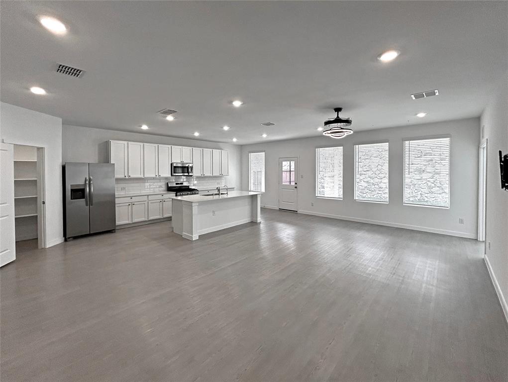 Open-concept living, breakfast nook and kitchen features white cabinetry, a center island, stainless steel appliances, recessed lighting, and luxury vinyl plank flooring