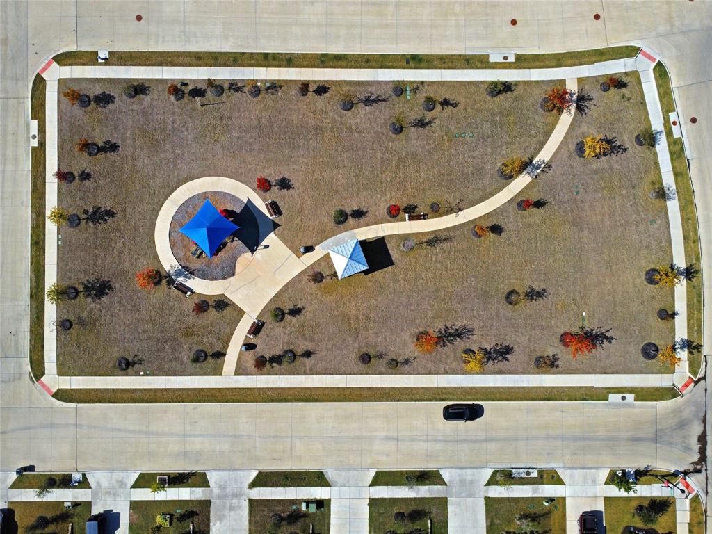 Aerial view of a community green space featuring concrete walking paths, a shaded structure, mature trees, and perimeter sidewalks
