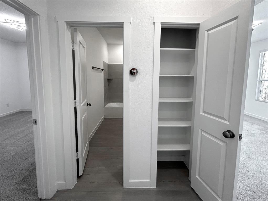A linen closet is beside the second bathroom between two of the secondary bedrooms. It features built-in storage shelving, two-panel interior doors, and solid luxury vinyl plank flooring