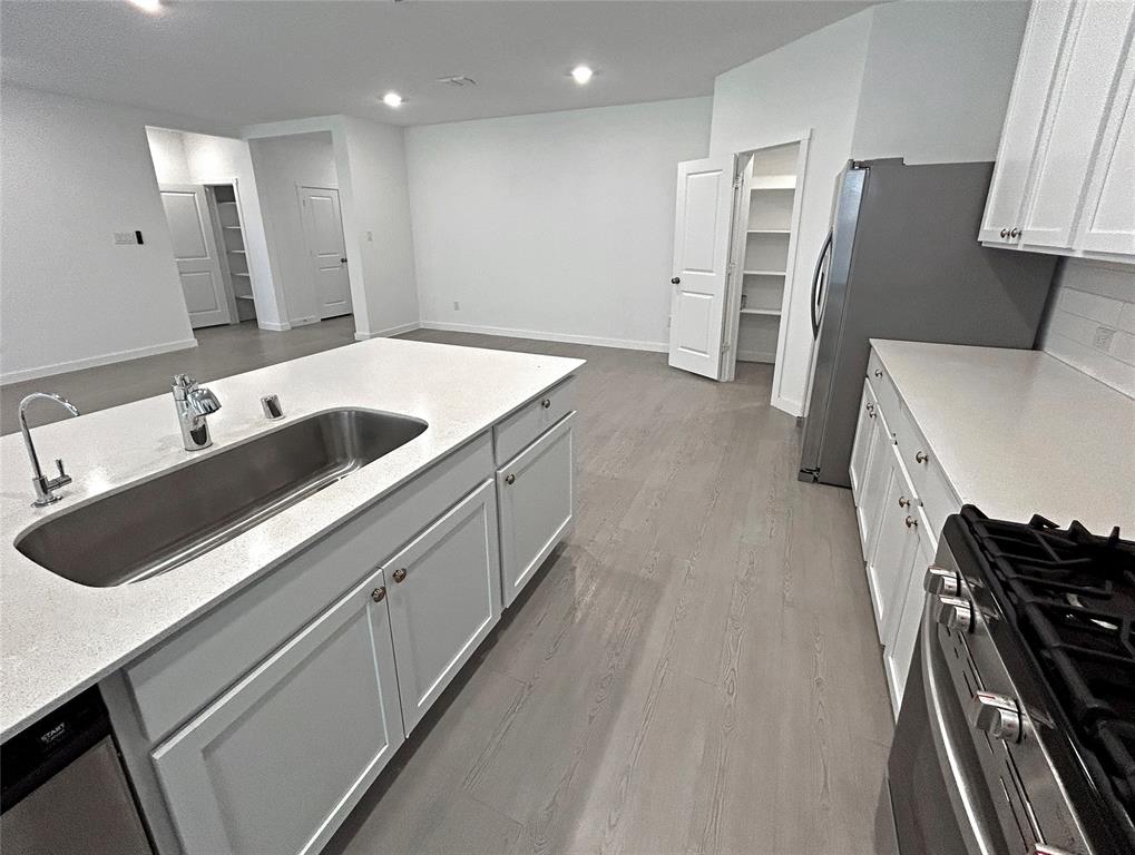 Kitchen featuring a central island with a stainless steel under-mount sink, quartz countertops, white shaker-style cabinetry, gas range, and luxury vinyl plank flooring