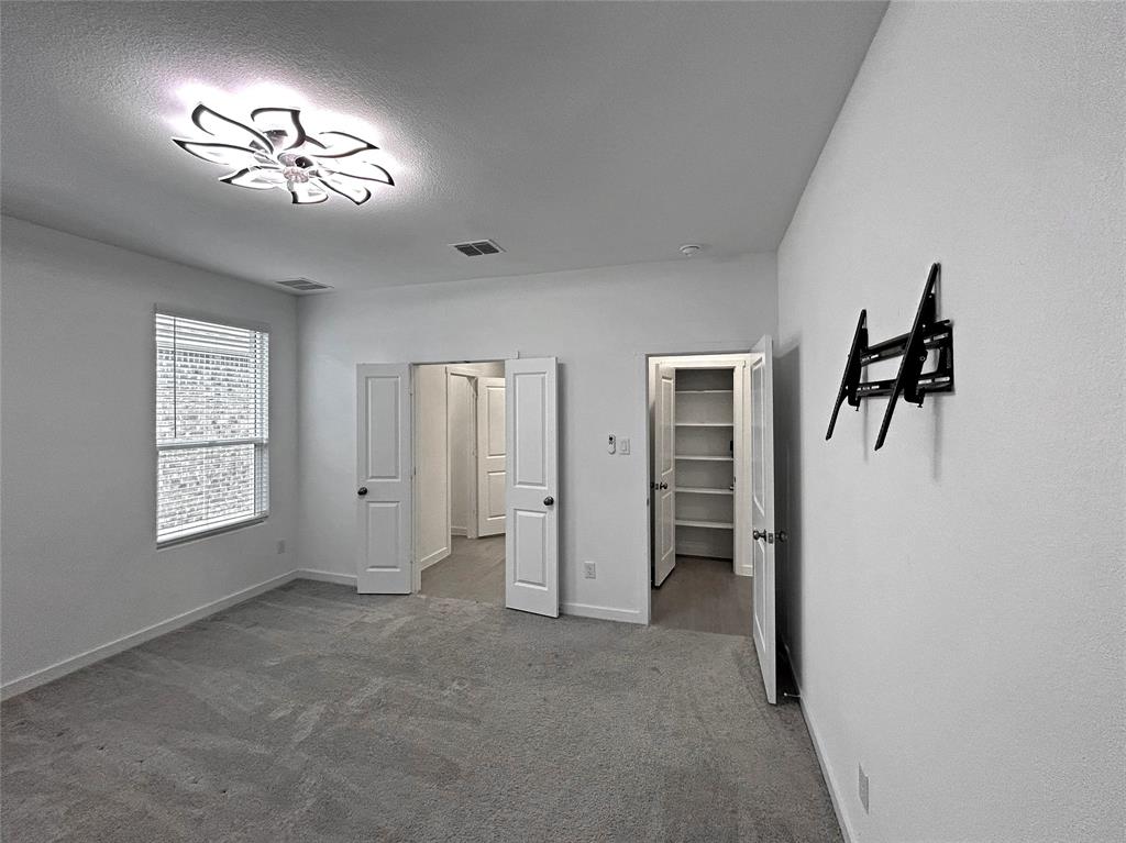 The primary bedroom features neutral carpet, a multi-paneled floral ceiling light fixture, a window with horizontal blinds, and a walk-in closet with built-in shelving