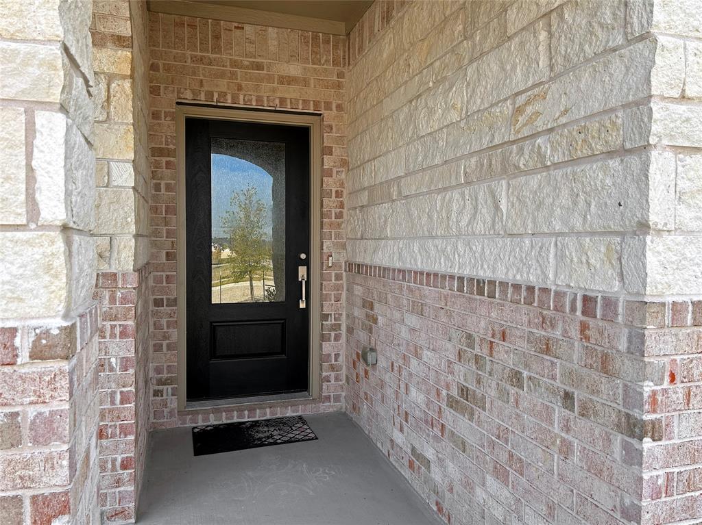 Covered entryway featuring mixed-masonry stone and brick facade, decorative solid-core front door with an integrated glass panel, and brushed metal hardware