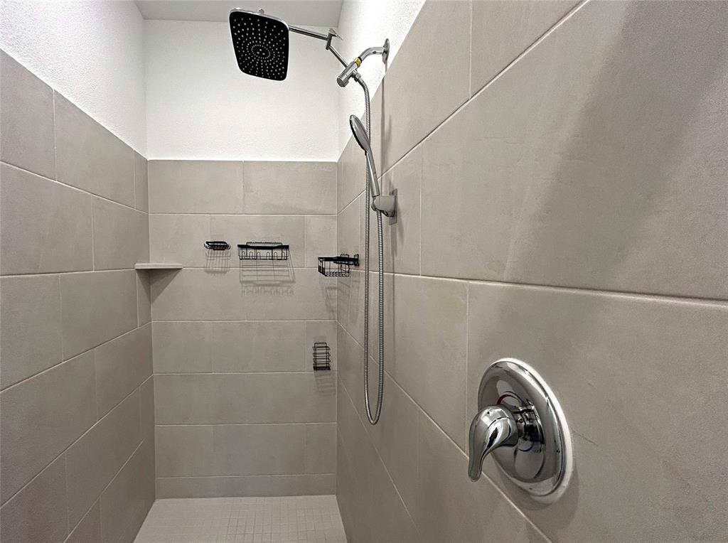 Walk-in shower featuring large-format ceramic tile surround, integrated rainfall showerhead, handheld shower wand, and polished chrome hardware