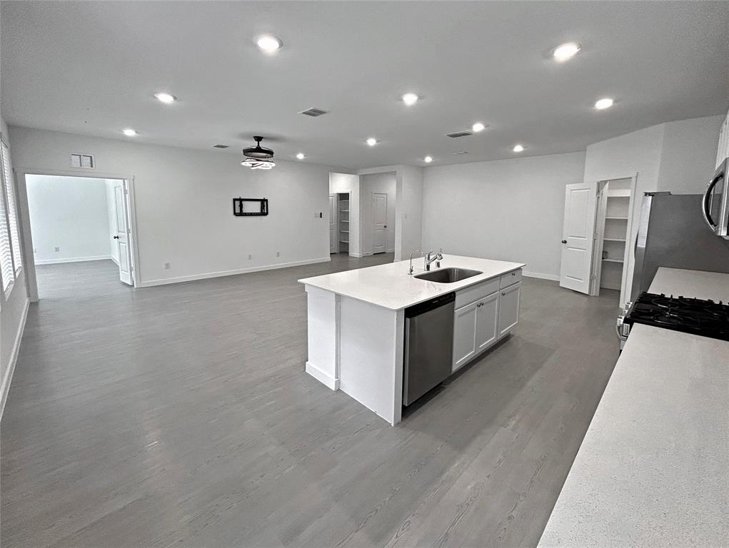 Kitchen features an island with a stone-finish countertop, stainless steel dishwasher, undermount sink, recessed lighting, gas range, and luxury vinyl plank flooring