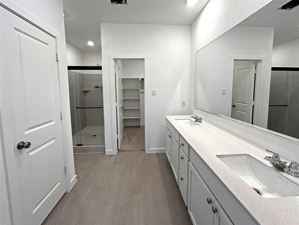 Dual vanity with stone-composite countertop, full-width wall mirror, walk-in shower with glass enclosure, and built-in closet shelving