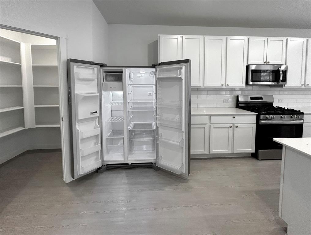 Kitchen featuring white shaker-style cabinetry, a subway tile backsplash, light-colored countertops, stainless steel appliances with a refrigerator, and a walk-in pantry with built-in shelving