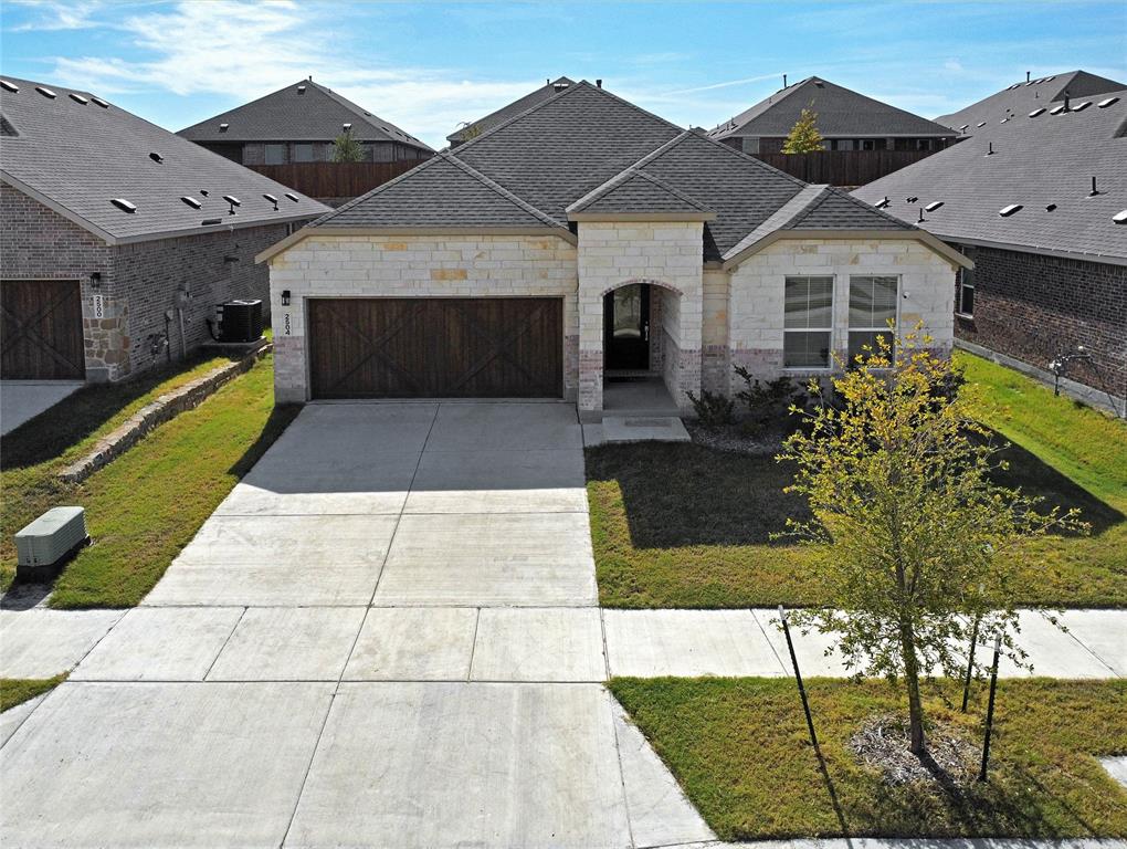 Stone veneer exterior features a dual-car garage with wood-finish decorative doors, asphalt shingle roofing, and a concrete driveway