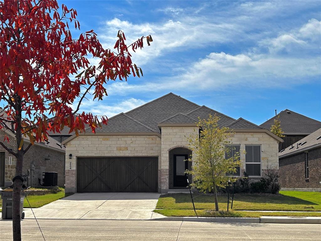 Single-story stone veneer exterior featuring a multi-gabled roofline, dark-toned carriage-style garage door with X-brace detailing, and a covered entryway