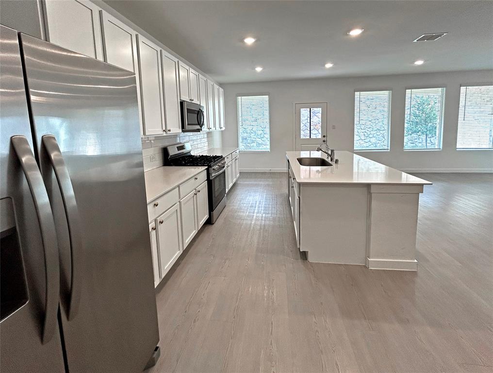 Kitchen featuring white cabinetry, solid-surface countertops, center island with undermount sink, stainless steel appliances, and luxury vinyl plank flooring