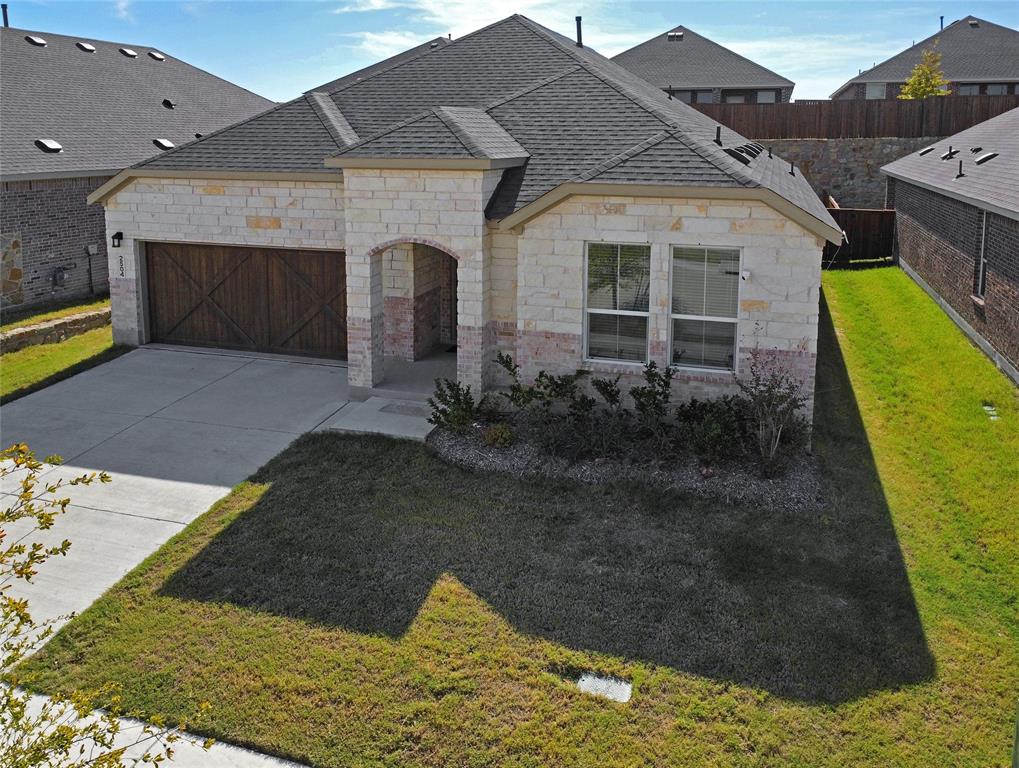 Stone veneer exterior, architectural shingle roof, arched covered entryway, and decorative wood-finish garage door with cross-buck detailing
