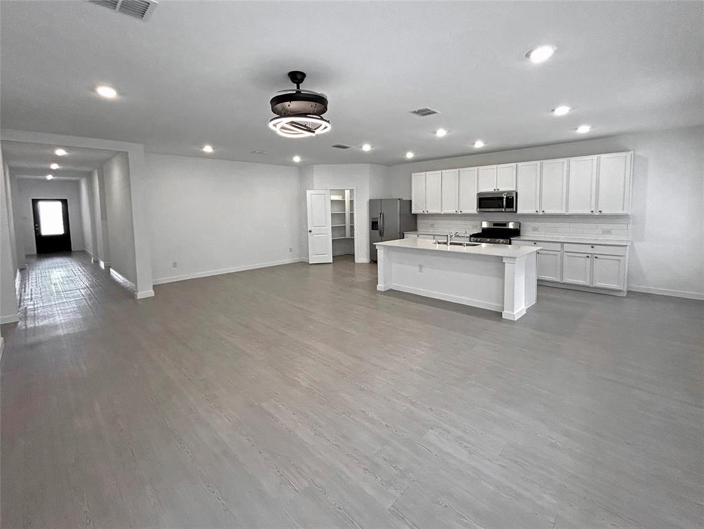 Open-concept interior featuring luxury vinyl plank flooring, recessed lighting, a kitchen island with stone countertop, white shaker-style cabinetry, and an enclosed pantry