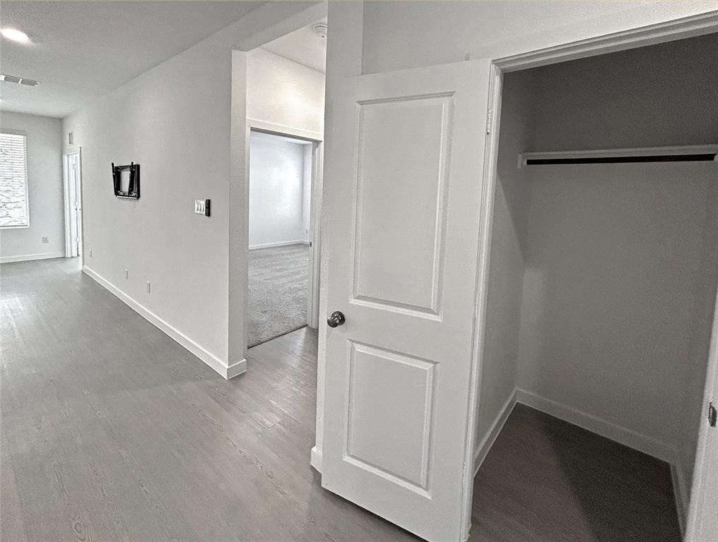 A hallway coat closet near the primary bedroom has luxury vinyl plank flooring, two-panel interior doors, and a closet with a built-in rod