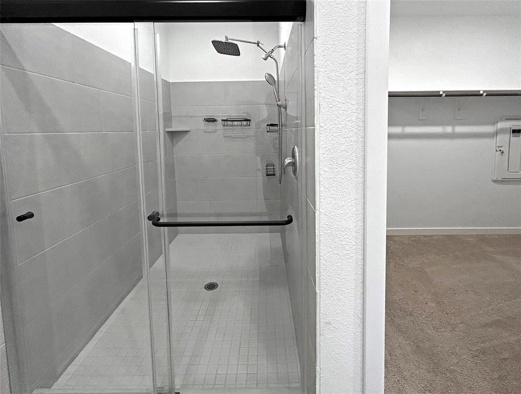 Walk-in shower featuring large-format wall tile, glass enclosure with matte black hardware, rainfall shower head, and adjustable handheld sprayer