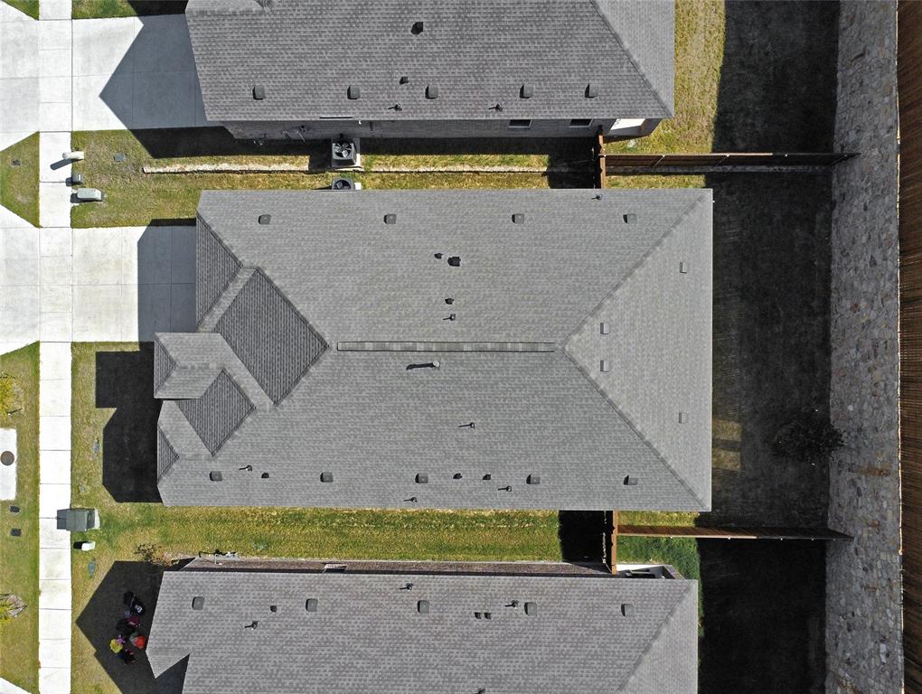 Aerial view of the residential property featuring a composition shingle roof, concrete driveway, and stone and wood perimeter fencing
