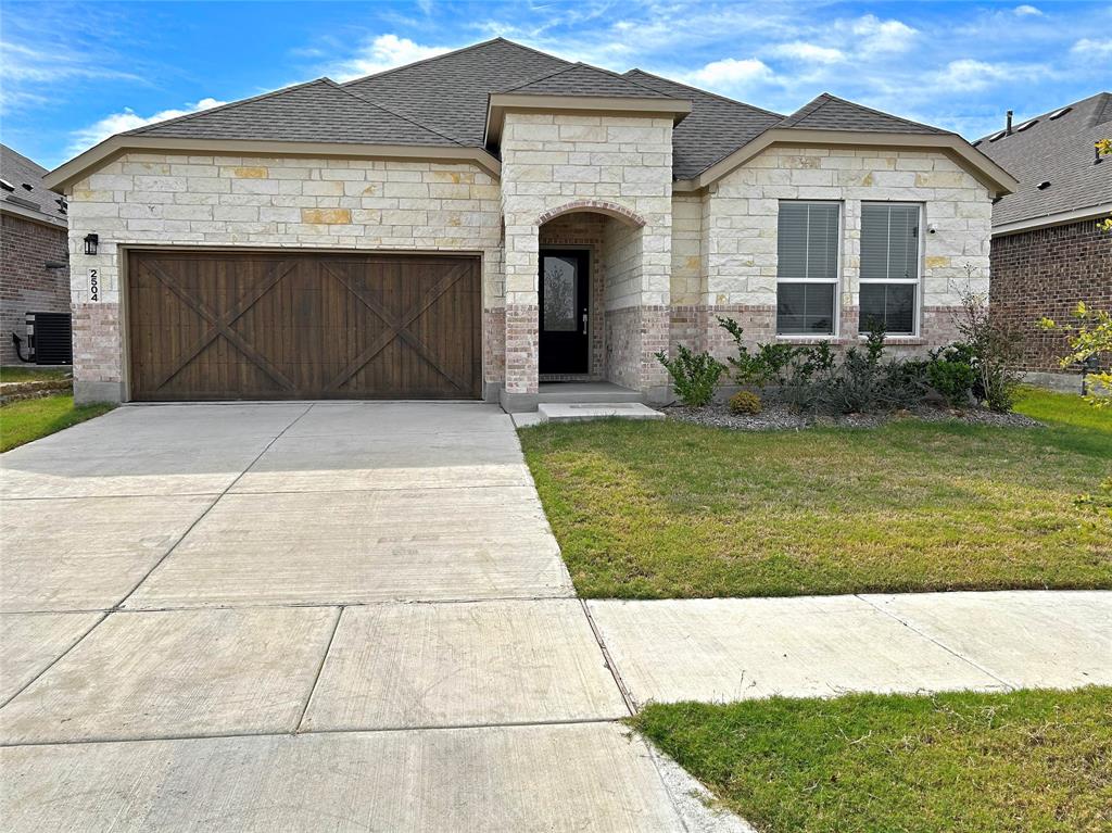 Single-story exterior featuring light-toned masonry, wood-finish garage door with X-brace detailing, multi-hipped roof, and concrete driveway