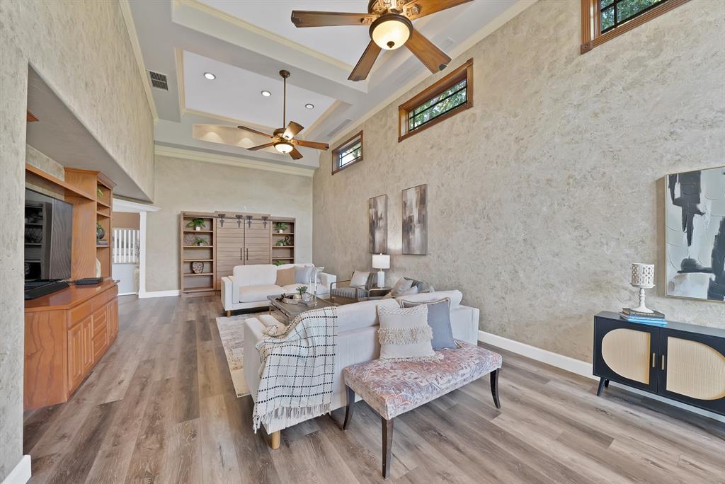 High ceilings with tray architectural detail, wood-finish flooring, built-in wooden cabinetry, transom windows, and dual ceiling fans