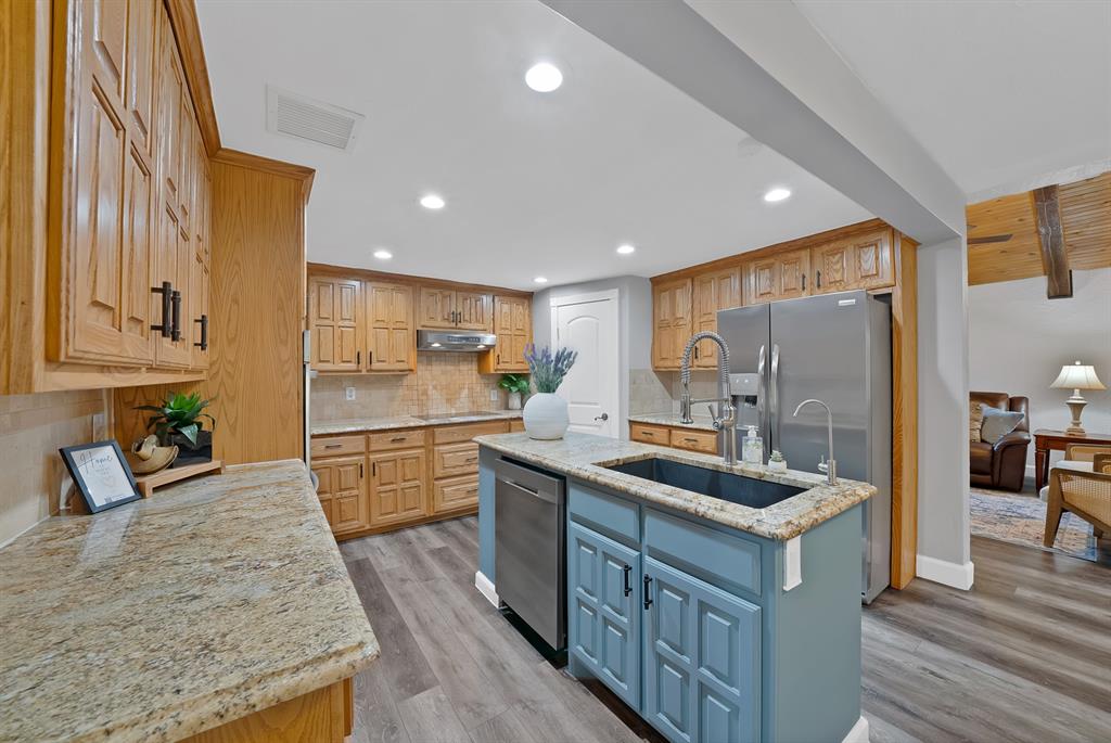 Kitchen featuring wood cabinetry, stone countertops, a contrasting blue center island with a drop-in sink, recessed lighting, and wood-finish flooring