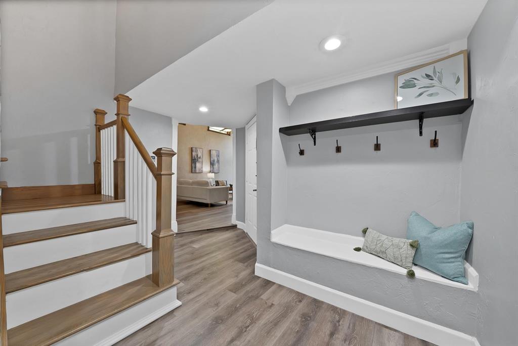 Entryway featuring wood-finish flooring, a built-in bench, wall-mounted coat hooks with a floating shelf, and a staircase with wood handrails and white balusters