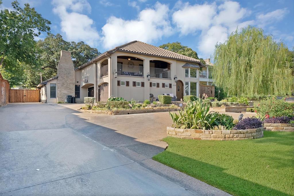 Stucco exterior featuring a second-story covered balcony, tile roof, exterior stone-finish chimney, and tiered stone landscaping walls