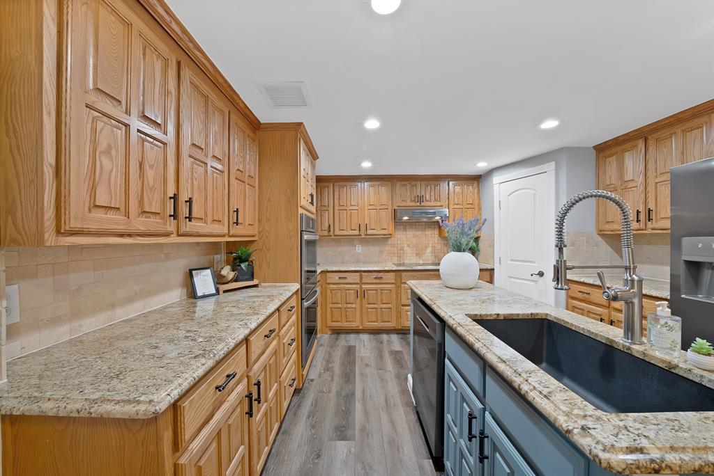 Kitchen featuring stained wood cabinetry, stone countertops, integrated wall oven, wood-finish flooring, and an undermount sink with a pull-down faucet