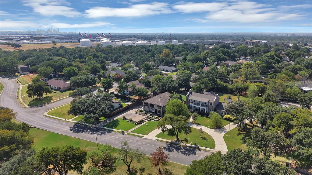 Aerial perspective of a multi-story residence featuring a circular concrete driveway, extensive tree canopy, manicured lawn, and large-scale hardscaping