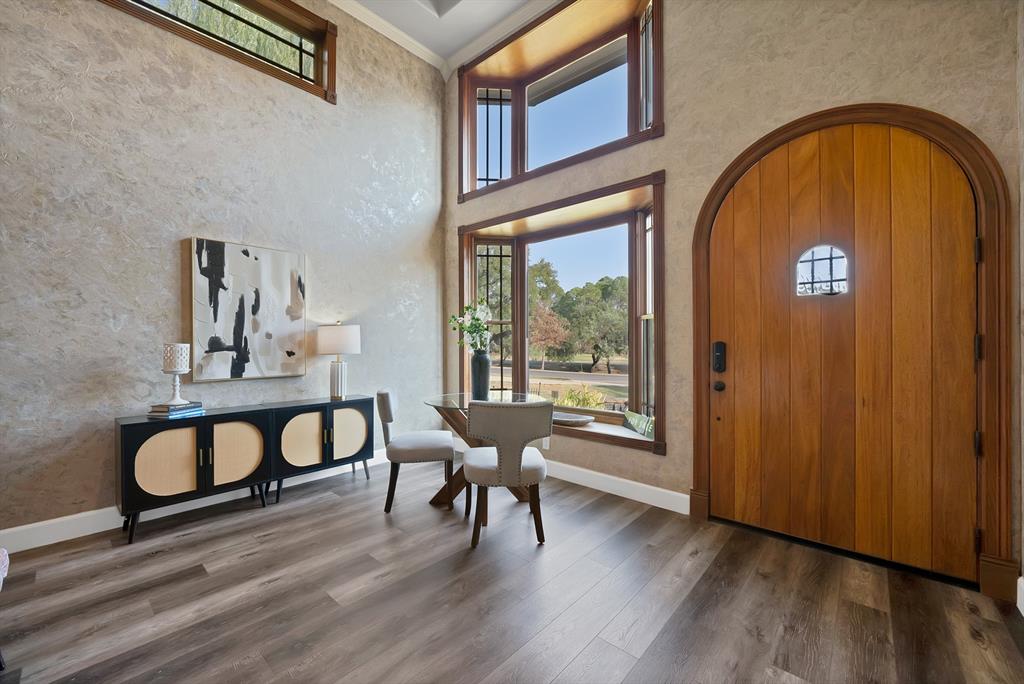 Vaulted ceiling foyer featuring a custom arched solid wood entry door, expansive bay windows, textured wall finishes, and wide-plank wood-finish flooring