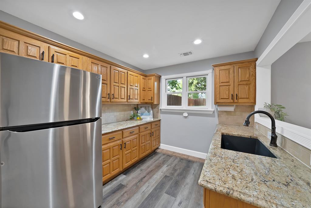 Kitchen featuring wood cabinetry, natural stone countertops, a stainless steel refrigerator, recessed lighting, and a black undermount sink with a gooseneck faucet